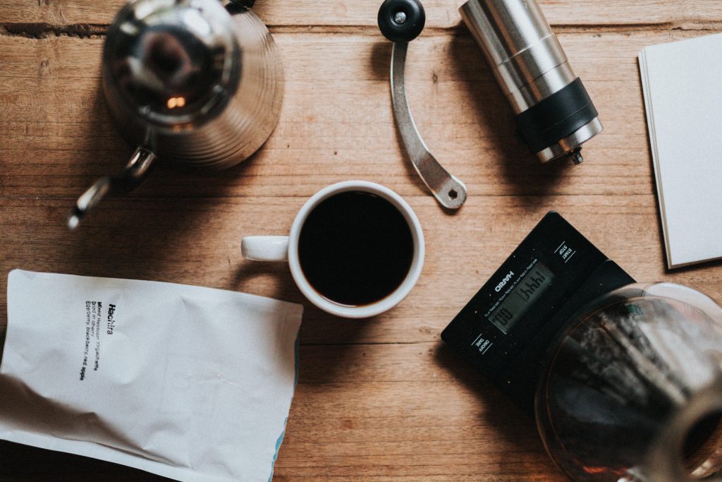 Une tasse de café noir à côté d'une balance, d'un sac de café torréfié, d'un moulin à main et d'une bouilloire.