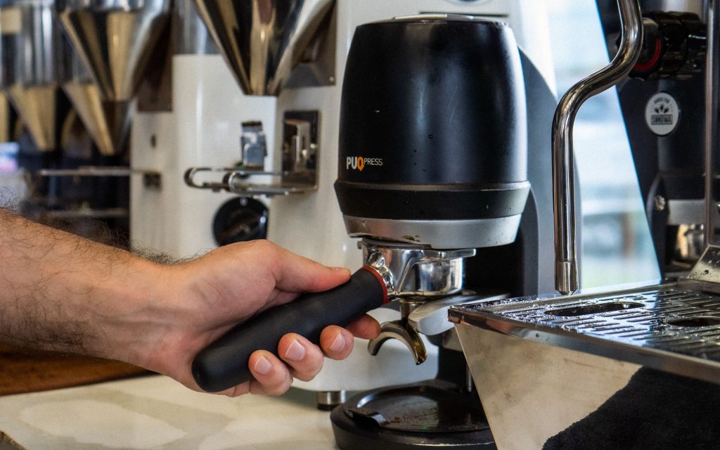 Un barista utilise un tamper automatique pour tasser le marc de café dans un portafiltre.